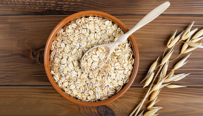 oat flakes in bowl with spoon near and ears on wooden table. Top view. Uncooked oatmeal