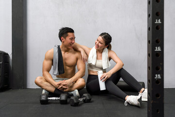 Young asian couple amidst workout on gym floor, surrounded by dumbbells, engaging in a moment of...