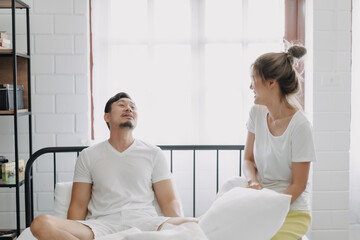 Obraz premium Asian wife and husband playing pillow fight funny and laugh on the bed.