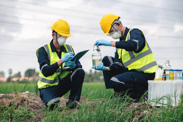 Two Environmental Engineers Inspect Water Quality and Take Water Samples Notes in The Field Near Farmland, Natural Water Sources maybe Contaminated by Toxic Waste or Suspicious Pollution Sites. - obrazy, fototapety, plakaty