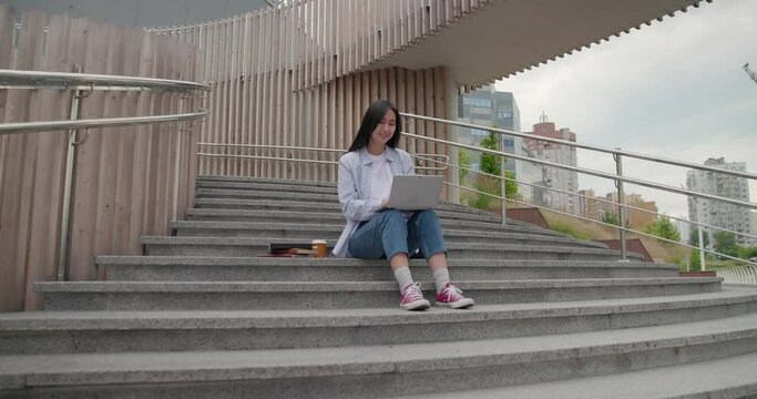 Young Asian woman student using laptop while sitting on a stairs outdoor