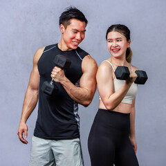 Portrait studio shot of strong fit young male and female muscular fitness model in sleeveless shirt sport bra and legging standing posing lifting weight metal dumbbells showing biceps together in gym