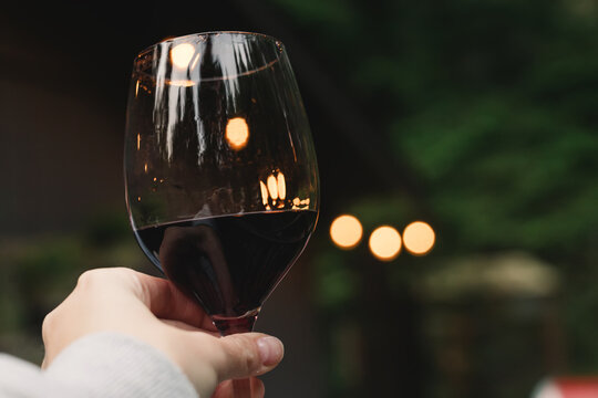 Woman holding a glass with red with blurred lights on the background, relax on the patio, cabin life