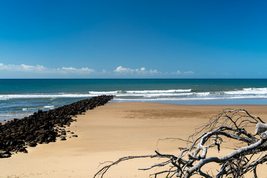 Sandy beach with rock wall extending into the sea. Bargara, Queensland, Australia.