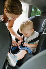 Mother fastening seat belt to her toddler boy in car