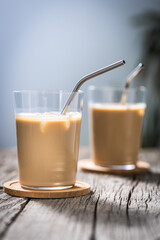 Ice coffee in transparent glass with straw, placed on rustic board. Popular summer coffee cocktail drink.