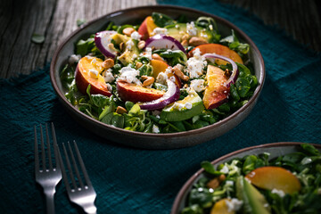 Salad with peach, onion, avocado, nuts and cheese, served on a plate in dark ambient. Healthy super food meal on wooden board.