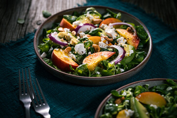 Salad with peach, onion, avocado, nuts and cheese, served on a plate in dark ambient. Healthy super food meal on wooden board.