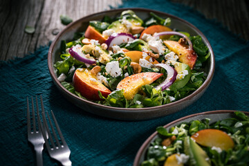 Salad with peach, onion, avocado, nuts and cheese, served on a plate in dark ambient. Healthy super food meal on wooden board.