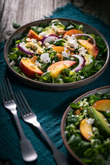 Salad with peach, onion, avocado, nuts and cheese, served on a plate in dark ambient. Healthy super food meal on wooden board.