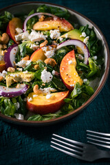Salad with peach, onion, avocado, nuts and cheese, served on a plate in dark ambient. Healthy super food meal on wooden board.