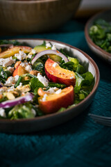 Salad with peach, onion, avocado, nuts and cheese, served on a plate in dark ambient. Healthy super food meal on wooden board.