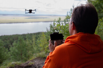 A man holds a remote control and controls a drone in a forest on a hill. The drone operator takes...