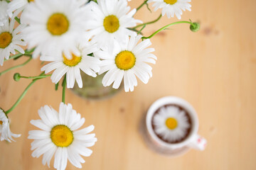 Chamomile tea is on the table next to a bouquet of daisies