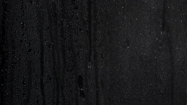 Rain drops on glass pouring down with normal speed on a black background