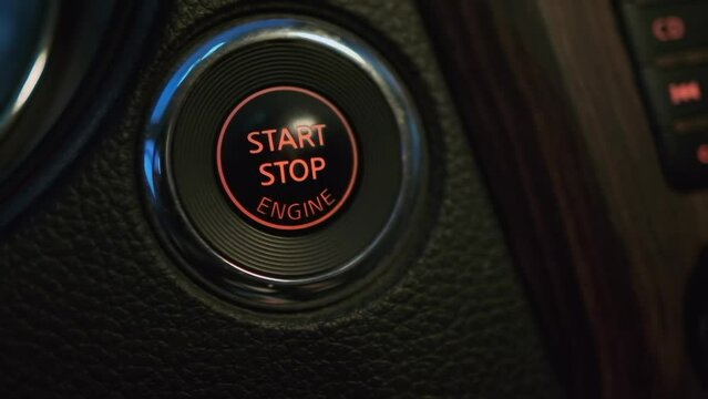 Man hand pushing start stop button in car, macro, close up, male hand starting car with button. Male driver using start button in modern car. Wood panel trim leather car interior. 