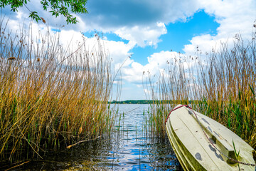 View of Lake Barleber with tall grass and a boat in the foreground. Lake near Magdeburg.
