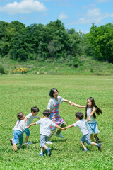 Obraz premium 草原で輪になって遊ぶ子どもたちと女性