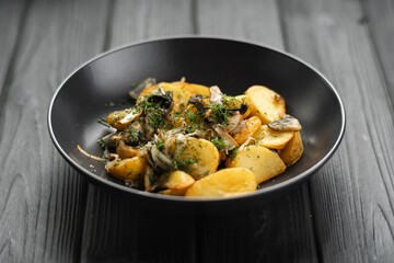 Fried potatoes with mushrooms and onions on a black wooden background, top view