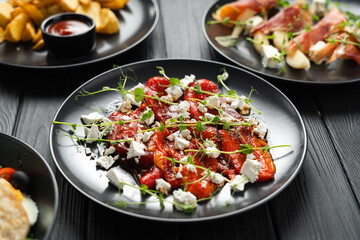 Baked red peppers with feta cheese and microgreens on a plate on a wooden table in a restaurant, close-up