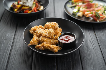 Fried crispy chicken nuggets with ketchup on a black plate on a wooden table in a restaurant, copy space
