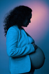 Fototapeta na wymiar Side portrait of a pregnant woman in stylish blazer, holding her naked belly, isolated over neon light color background