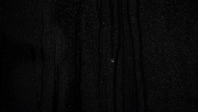 Many Rain drops running down on glass on a black background