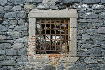 Stone wall house with collapsed roof. Window with rusty bars and light. Ruins.