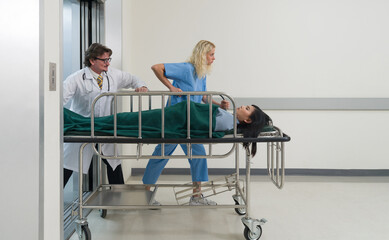A nurse and doctor in propels a wheeled stretcher, carrying a patient through the sterile, well-lit...