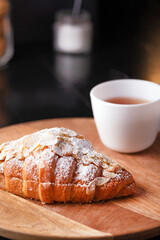 fresh croissant with powder on a wooden stand with a cup of tea on a dark background