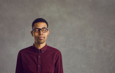 Obraz premium Young skeptical African American man suspiciously looks to the side on a gray concrete background. Man with a distrustful expression looks in the direction of free space for text. Banner.