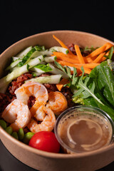 Bowl with shrimps, carrots, cucumbers, beans and vegetables with herbs, on a black background. Healthy food concept