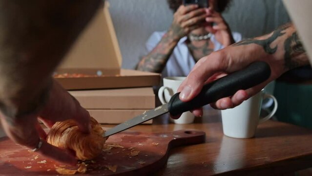 A man is in the kitchen slicing a croissant.