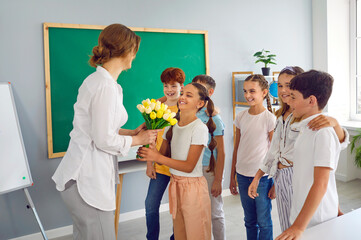 Smiling children give the teacher a bouquet of flowers for the holiday. Teacher's Day celebration in the classroom on the background of the blackboard. A woman holds a bouquet of tulips in her hands.