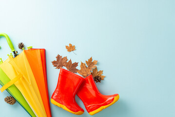 Protective attire for children in rainy weather. Frame a top view picture exhibiting colorful umbrella and red galoshes on blue isolated background, inviting text or advert incorporation