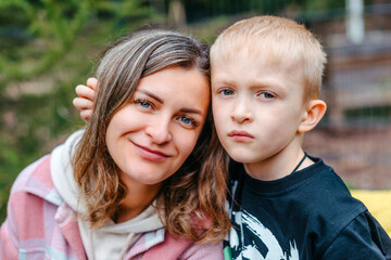 Mother and son outdoor lifestyle portrait in a park setting. Young mother with her seven years old little son are posing. Selective focus. Casual lifestyle photo.