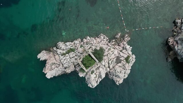 Top down aerial view big stone with old building in the sea next to Przno city in Montenegro, people swim in the sea , summer sunny day.