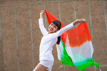 Indian little girl child waving tricolor cloth or odhani and celebrate national festival.