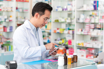 Professional pharmacist asian man smiling at counter using digital tablet for check medicine inventory in drug store, Medical service online, Telemedicine to giving medical information to patient.