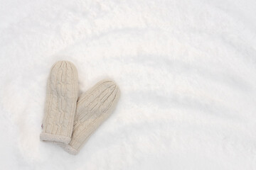 warm knitted mittens on snow, winter background, free space for text