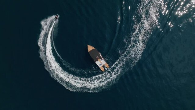 jet surfer riding around in the circle and making beautiful doughnuts around speed boat. top down aerial view. 