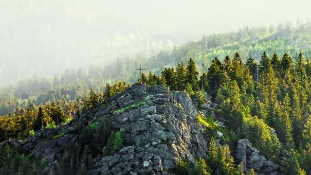 Drone shot of cross on rocky mountain surrounded with trees.