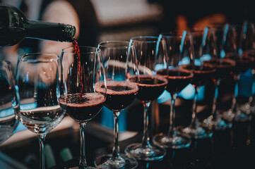 Party and celebration concepts. Bartender pours red wine in glasses at bar. Male sommelier pouring red wine into long-stemmed wineglasses. - obrazy, fototapety, plakaty