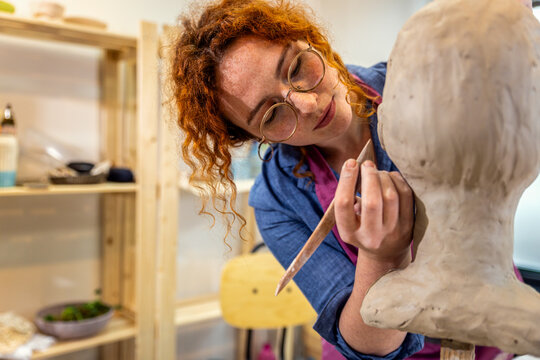 Female sculptor working in pottery studio workshop sculpting human head.