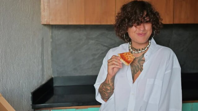 A woman in the kitchen eating pizza