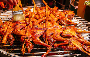 Grilled chicken wing with bamboo skewers on stove with charcoal,hands of seller cooking with brushes the sauce on the chicken.Close-up of Roast chicken barbecue.Delicious Asian Cuisine.