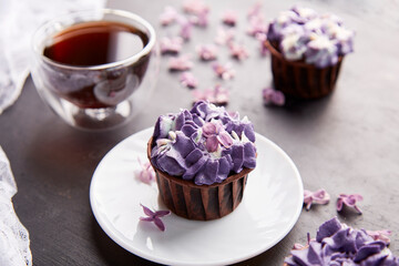  Aesthetics purple trendy floral cupcakes with cup of coffee. Violet sweet no sugar dessert among lilac flowers