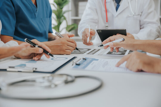 Medical analysts and physicians consult documents on graphs, data and charts in a hospital conference room. - Powered by Adobe