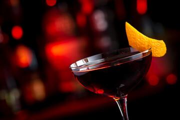 Adonis alcoholic cocktail drink with sherry and red vermouth, black bar counter background, steel tools and bottles
