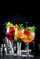 Red, white, rose sangria summer alcoholic cocktail drinks with spanish wine, fruits, citrus and ice. Black bar counter background, steel bar tools and bottles